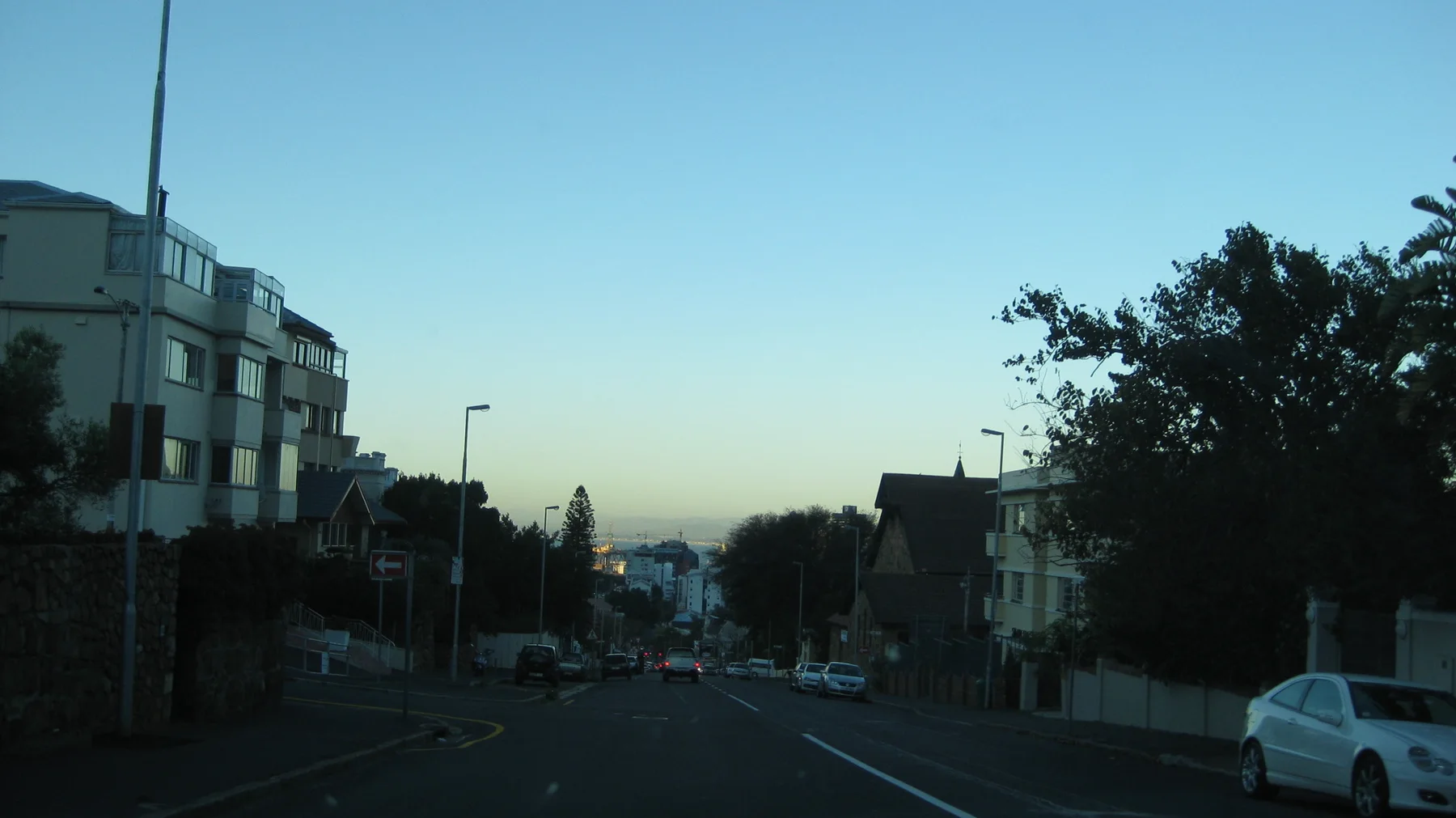 Low evening light falls between buildings along a city road.