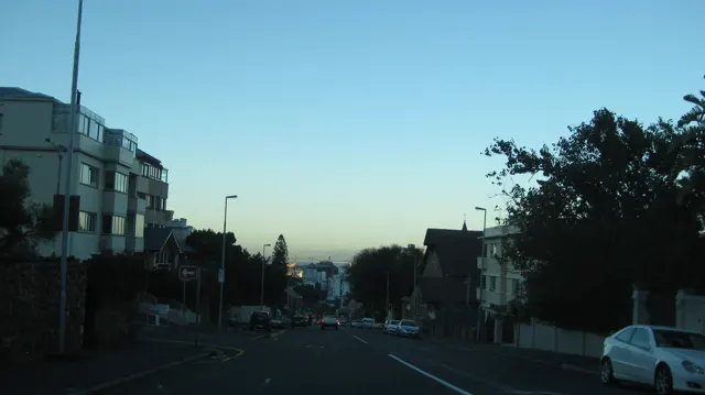 Low evening light falls between buildings along a city road.
