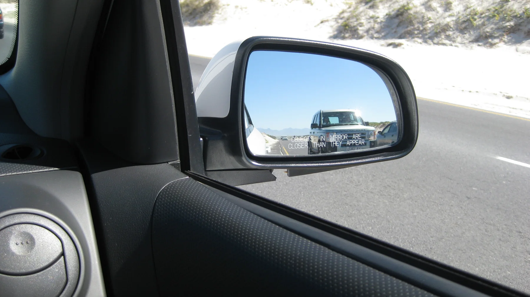 A following car appears in a vehicle's side mirror.