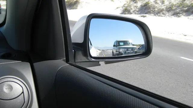 A following car appears in a vehicle's side mirror.