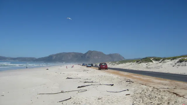 A road follows a broad sandy beach toward distant hills.
