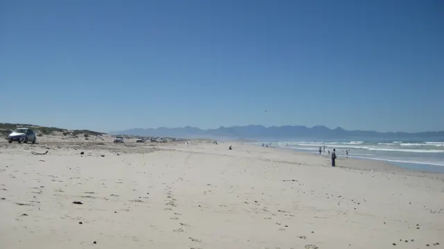 A broad beach stretches toward distant mountains with scattered walkers.