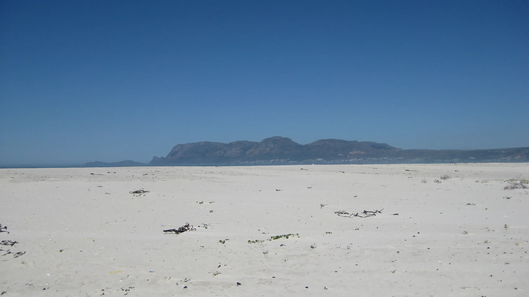 An empty sandy beach faces a distant mountain ridge.