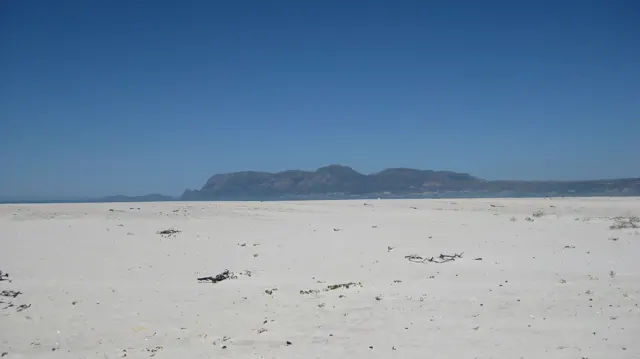 An empty sandy beach faces a distant mountain ridge.