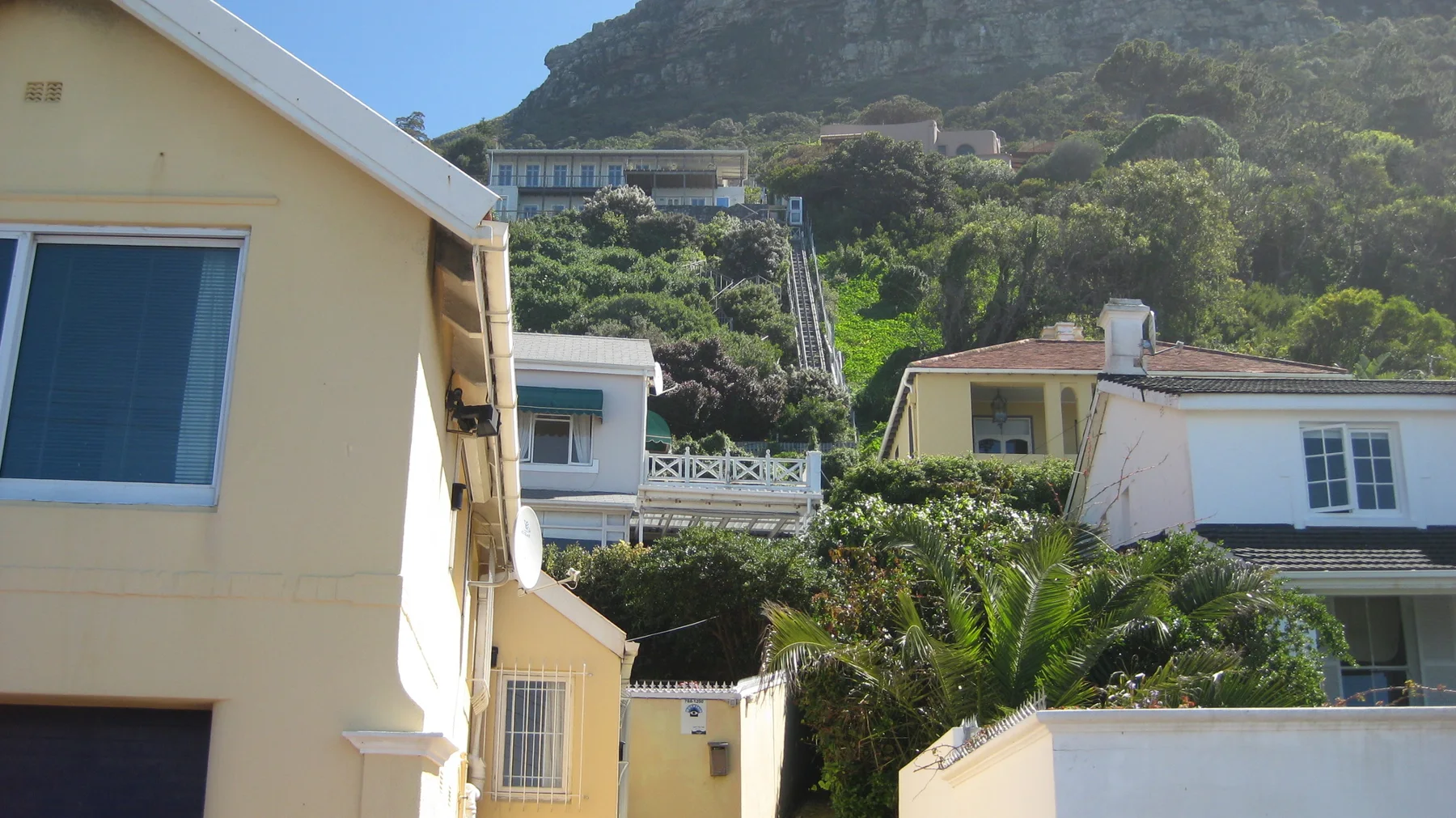 Pale yellow houses stand among trees on a steep green slope.