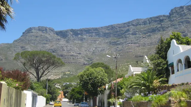A narrow residential street runs below a towering rocky ridge.