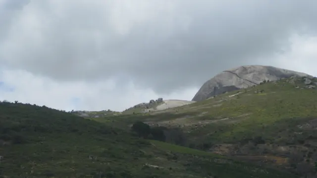 A pale rocky peak rises above green slopes beneath gray clouds.
