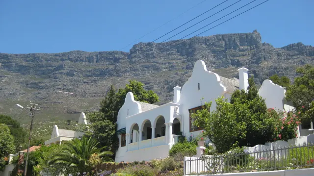 White curved gables stand below a broad rocky mountain wall.