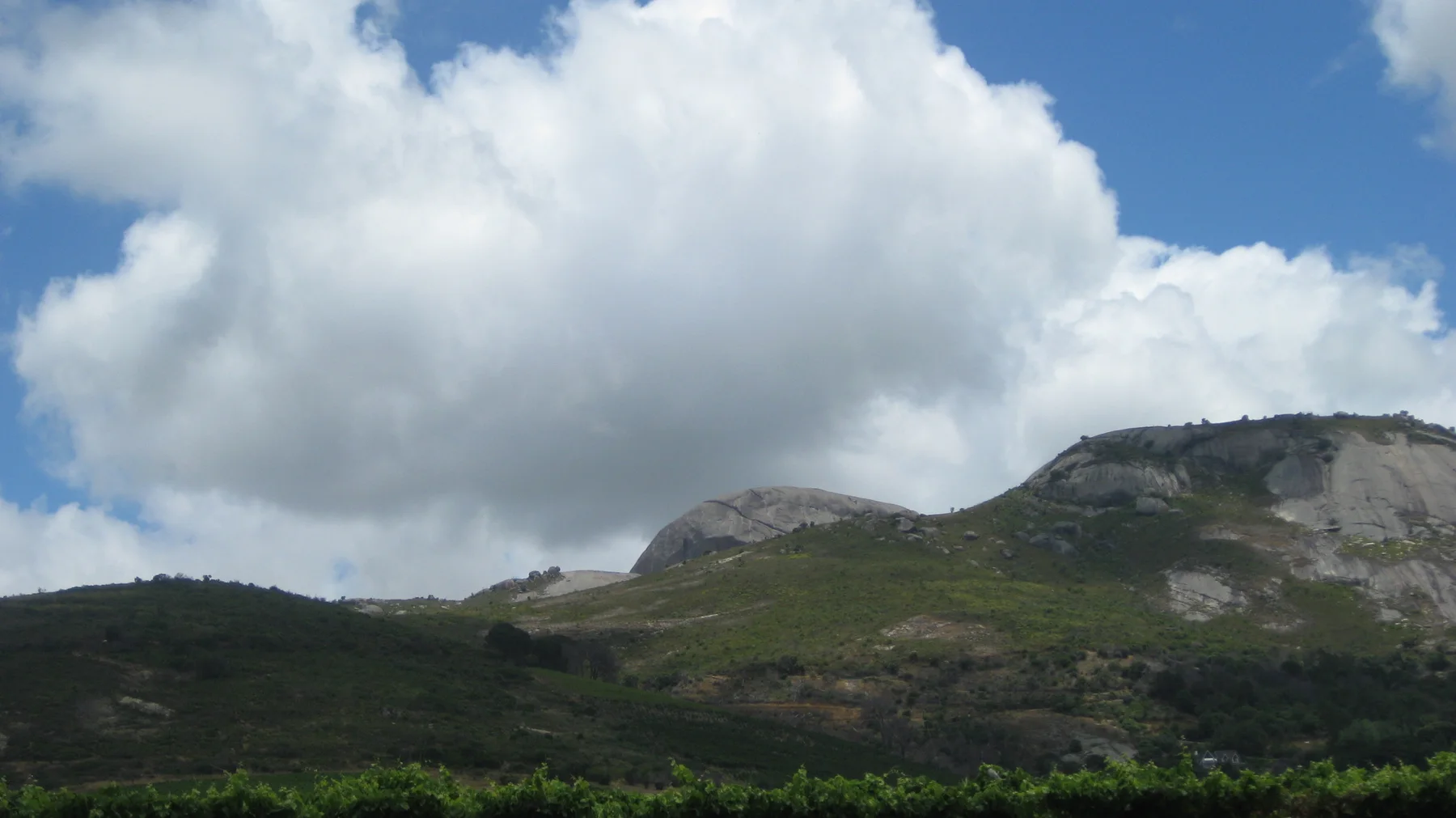 Large white clouds rise above low green hills and pale rock.
