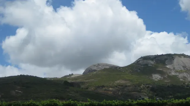 Large white clouds rise above low green hills and pale rock.