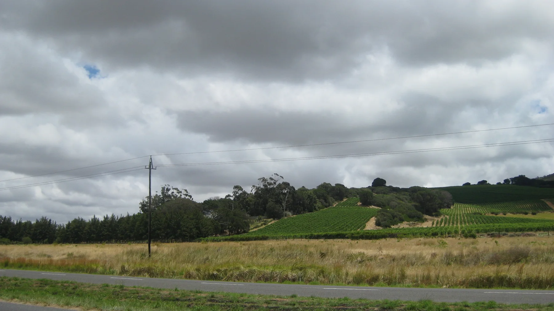 Green fields and scattered trees lie beneath heavy dark clouds.