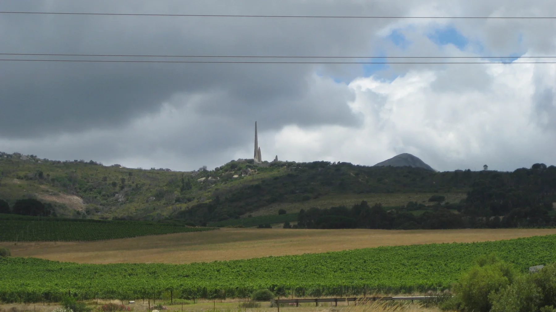 Cultivated fields lie below a hill with a distant slender spire.