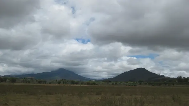 Two hills rise beyond open fields under heavy clouds.