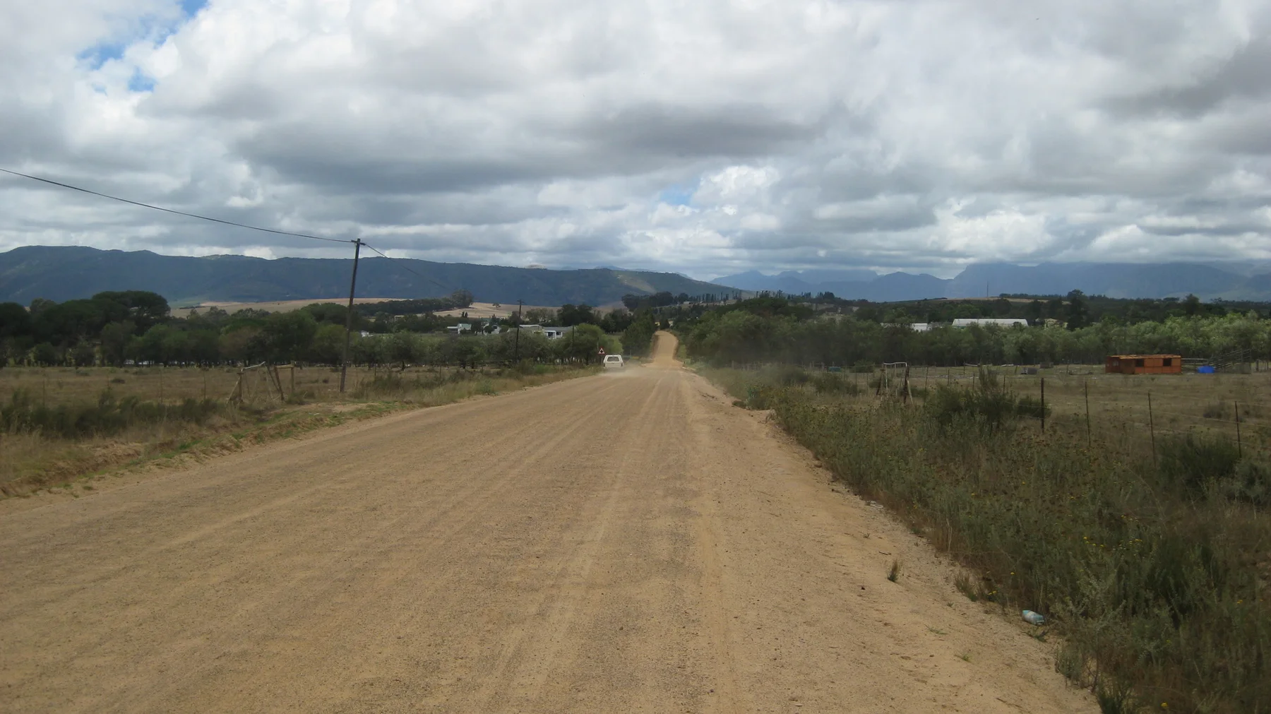 A broad dirt road crosses farmland toward distant mountains.