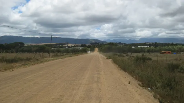A broad dirt road crosses farmland toward distant mountains.