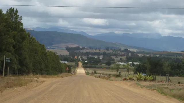A dirt road drops toward a long straight track through farmland.