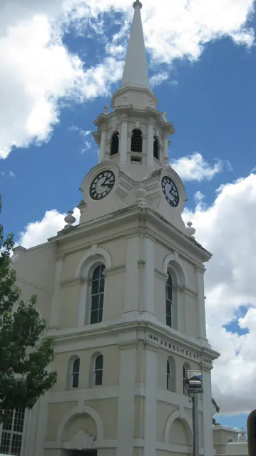 An ornate white clock tower and spire rise against broken clouds.