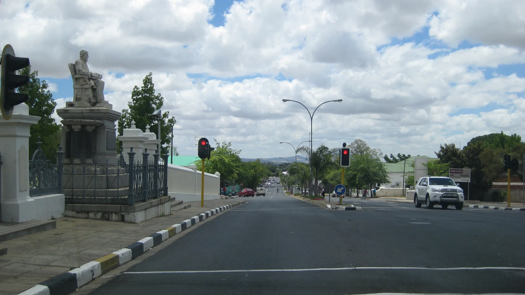 A stone monument stands beside traffic lights and a broad road.