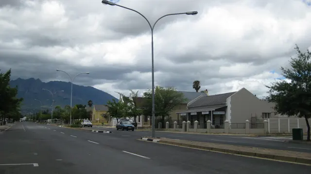 A twin-armed streetlight rises above a quiet street and low buildings.