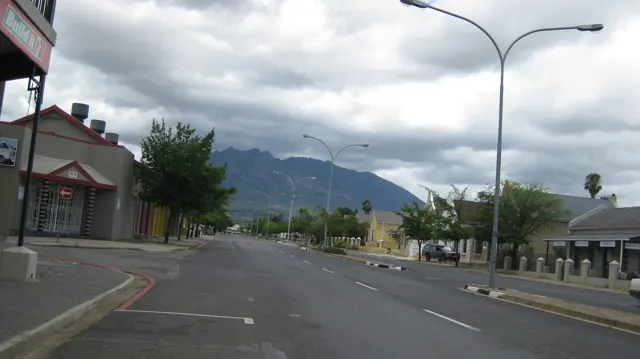 A broad street leads past low buildings toward clouded hills.
