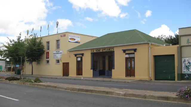 An ochre building with a green roof stands beside a quiet street.