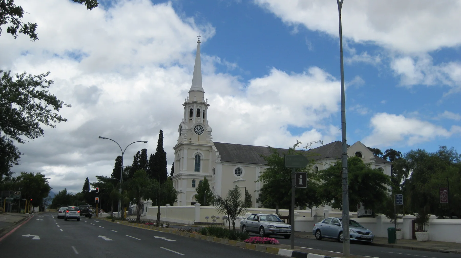 A white church and tall spire stand beside a broad town street.