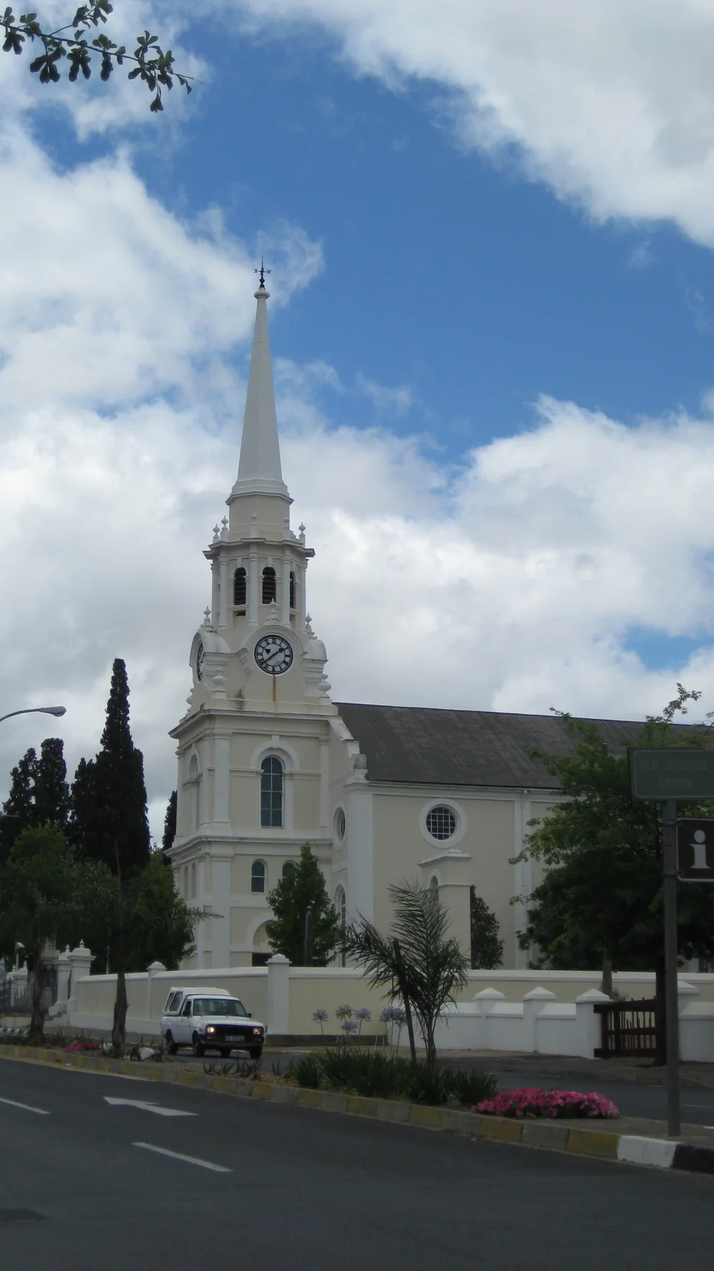 A tall white spire rises beside trees under a partly blue sky.