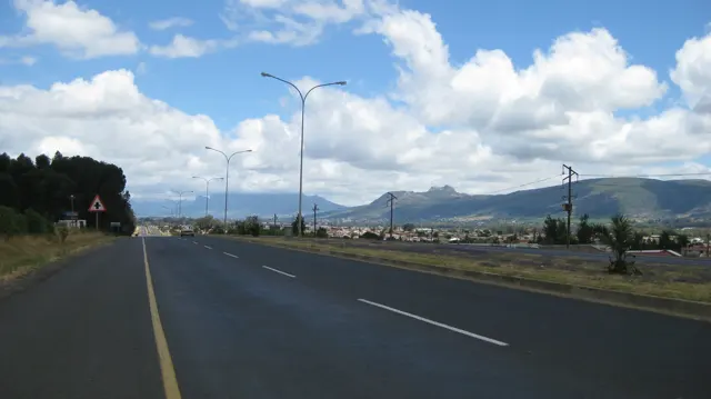 A road leads toward a mountain ridge beneath bright clouds.
