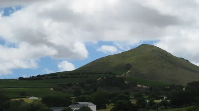 A rounded green hill stands above small houses and trees.