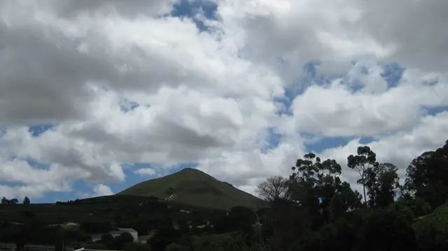 A low green hill sits beneath large white and gray clouds.
