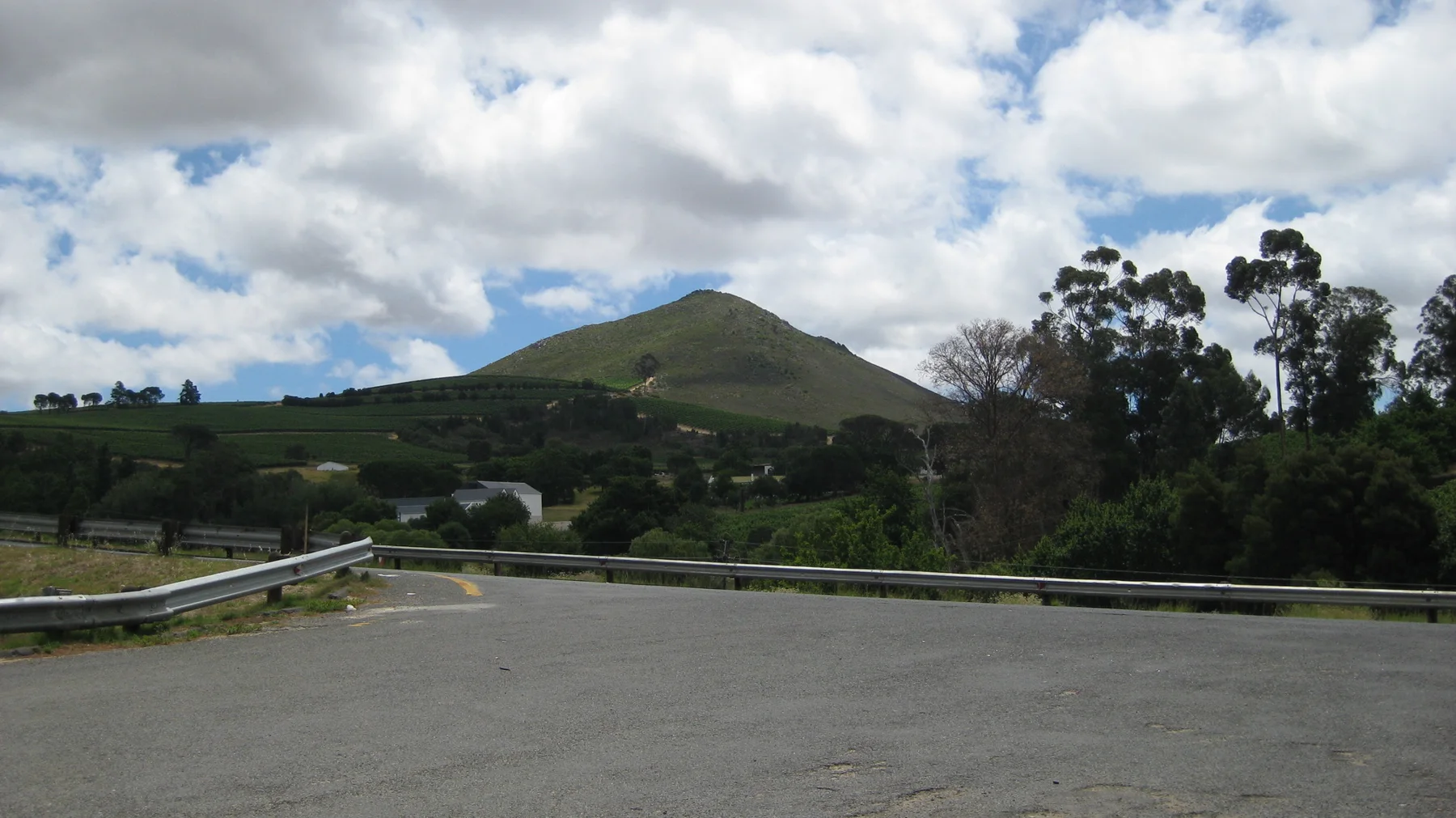 A broad road bend overlooks houses beneath a green hill.