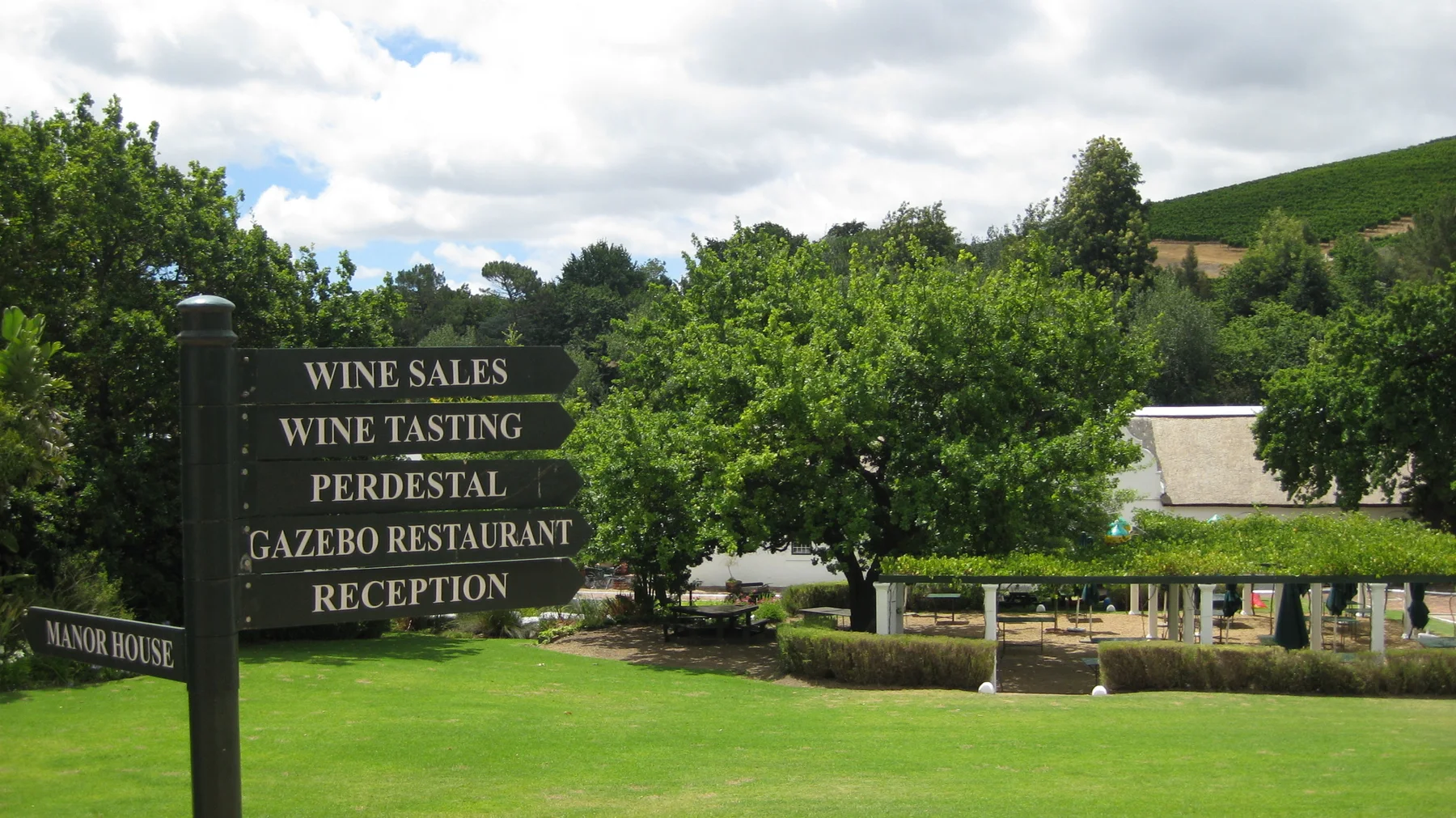A dark direction board lists wine tasting and other facilities beside a lawn.