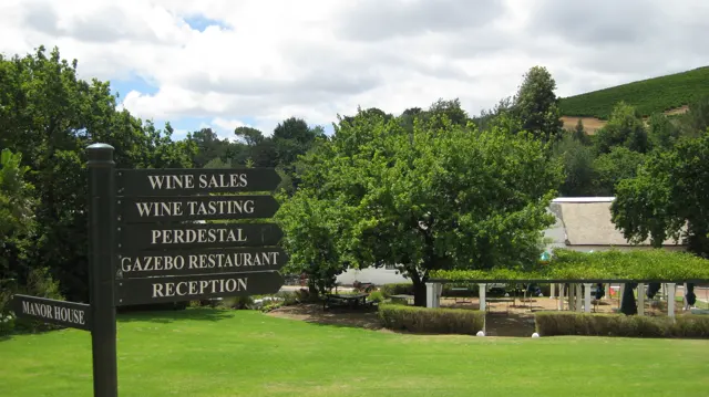 A dark direction board lists wine tasting and other facilities beside a lawn.