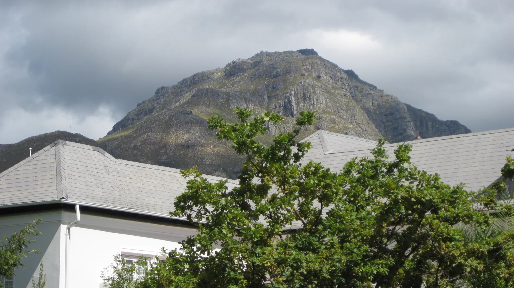 A rocky peak rises behind gray roofs and leafy branches.