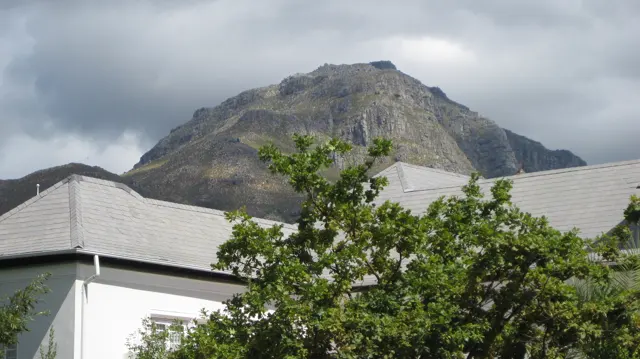 A rocky peak rises behind gray roofs and leafy branches.