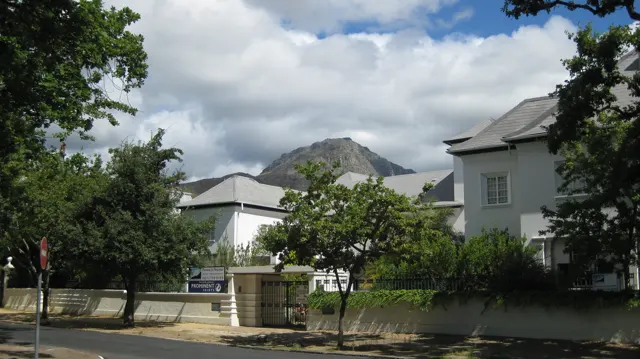 White buildings sit among trees with a rocky mountain beyond.