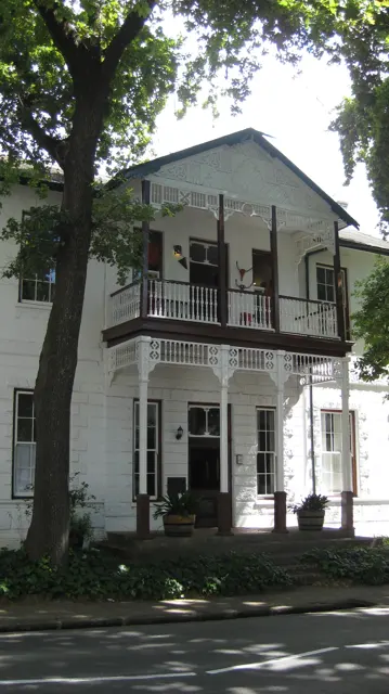A dark balcony projects from a white building behind a tree.