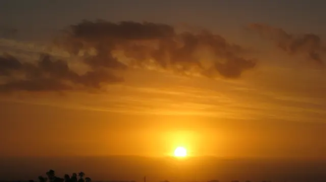 A low sun shines beneath a dark band of cloud.