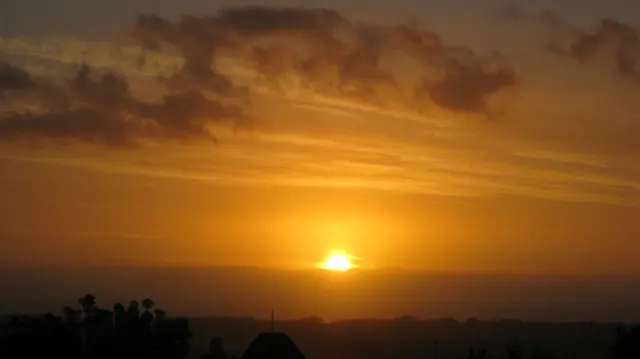 A low sun touches the horizon beneath golden cloud streaks.