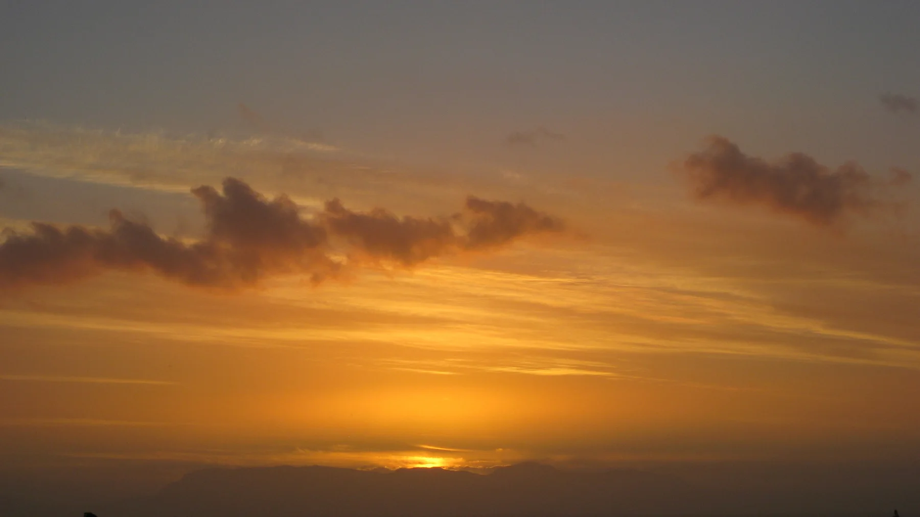 Golden afterglow spreads below darker clouds as the sun drops.