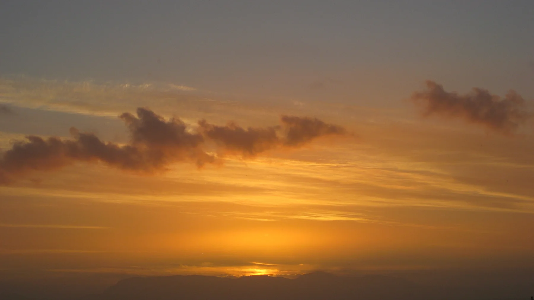 A small bright glow remains below layered orange clouds.