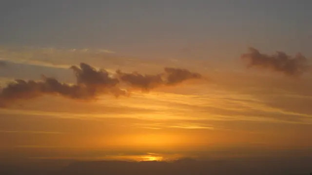 A small bright glow remains below layered orange clouds.