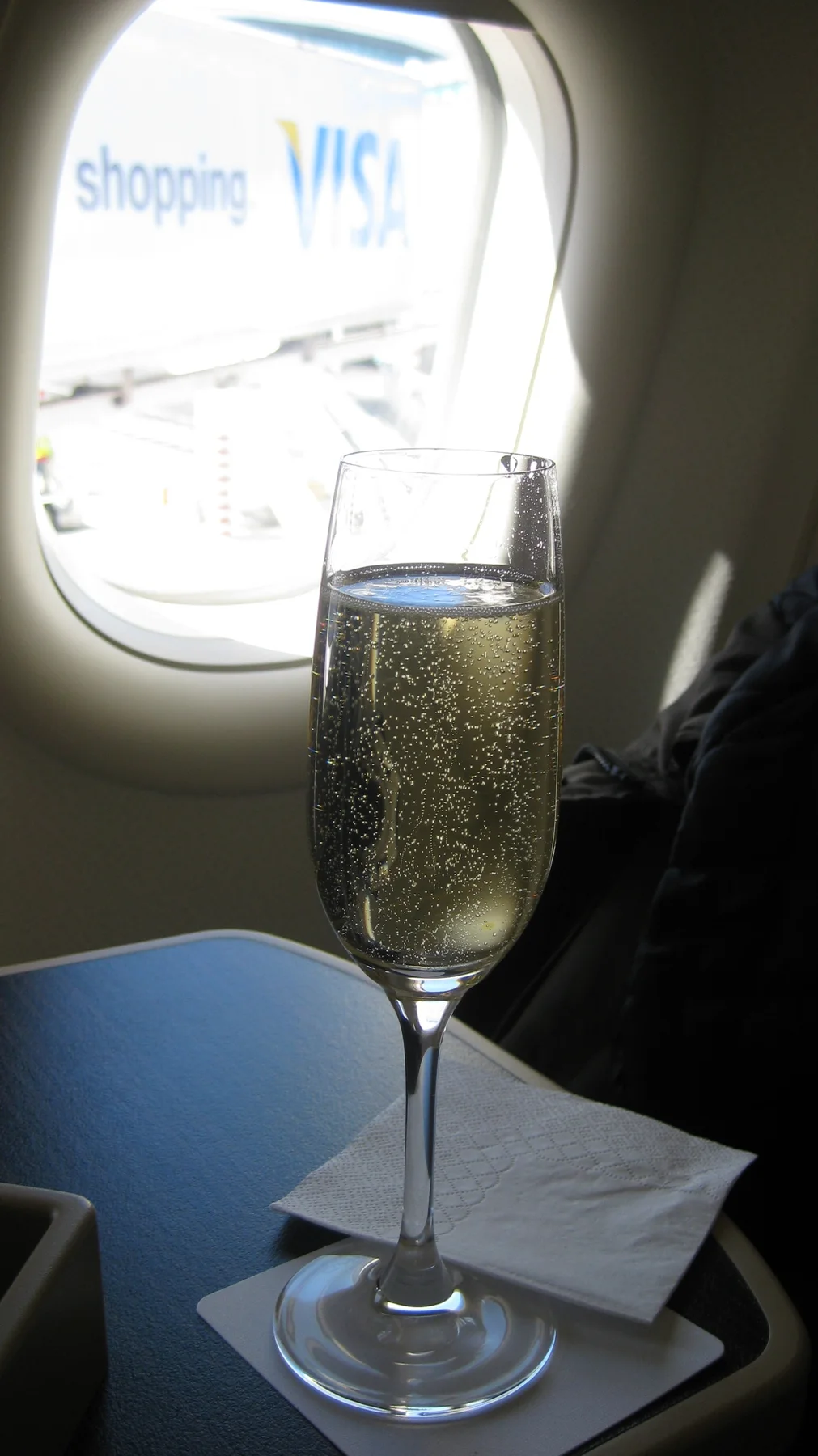 A flute of pale drink stands beside an aircraft window.