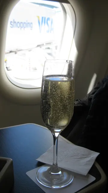A flute of pale drink stands beside an aircraft window.