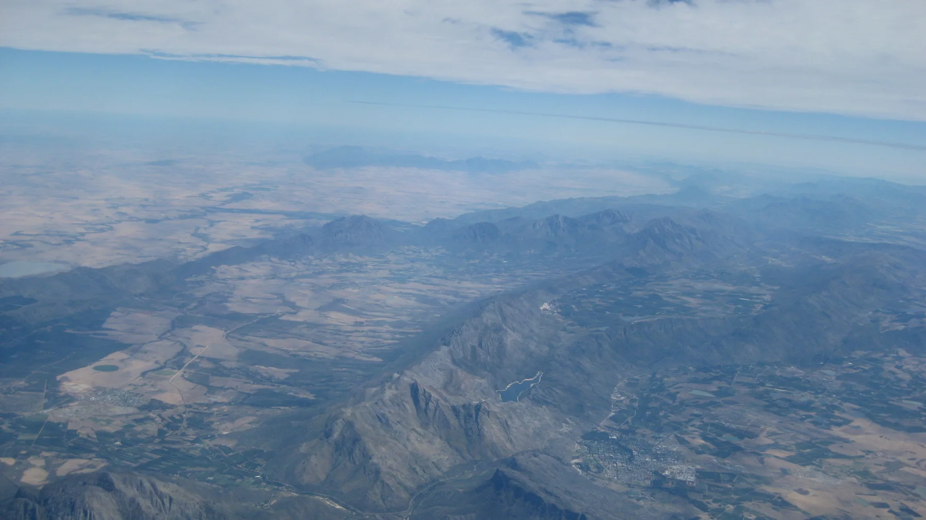 Mountain ridges and patchwork fields spread beneath aerial haze.