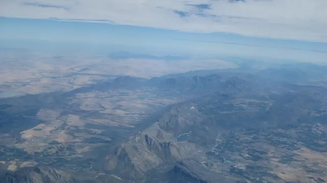 Mountain ridges and patchwork fields spread beneath aerial haze.