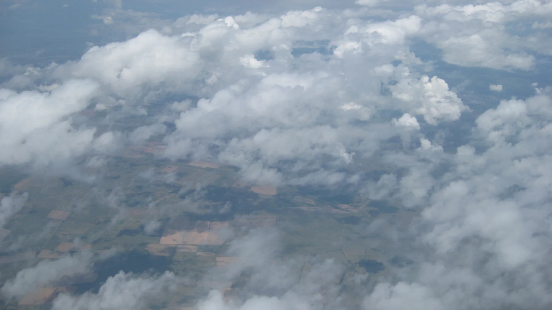 Gaps in broken clouds reveal land far below.