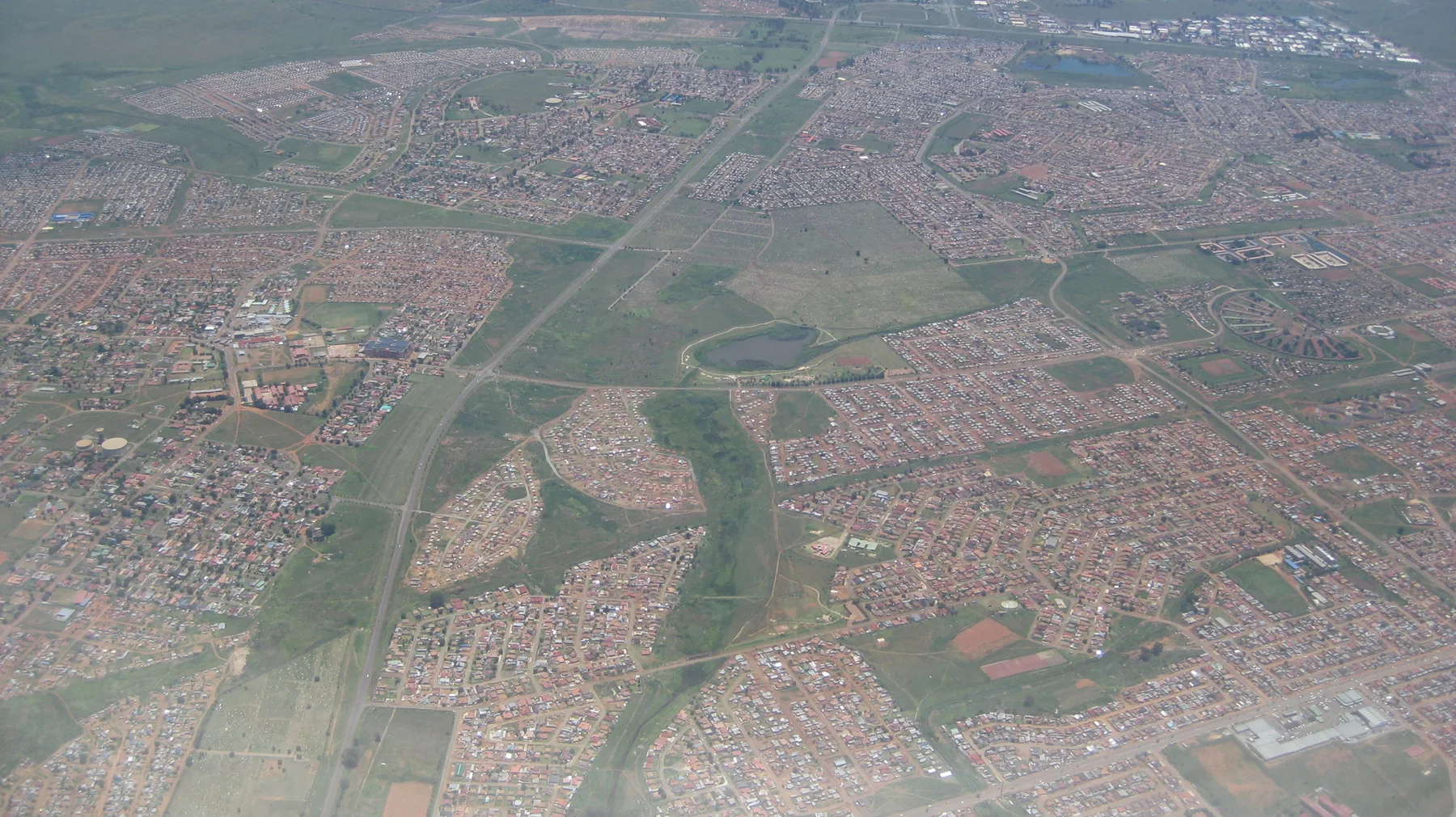 Dense neighborhoods spread around green open spaces in an aerial view.