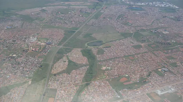 Dense neighborhoods spread around green open spaces in an aerial view.