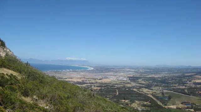 A green hillside overlooks a developed plain and distant bay.